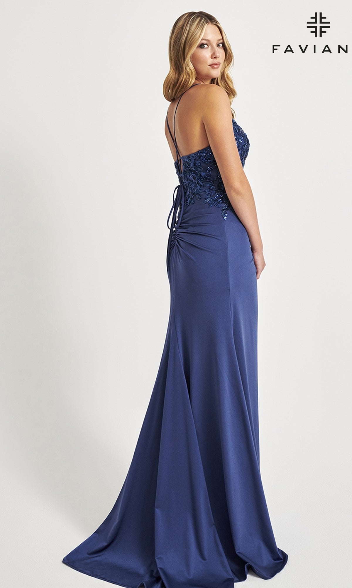 A woman models the Sequin-Applique Faviana Long Prom Dress 11018— a navy blue, floor-length gown with lace details, sequin appliques on the bodice, and thin straps—before a plain background featuring the